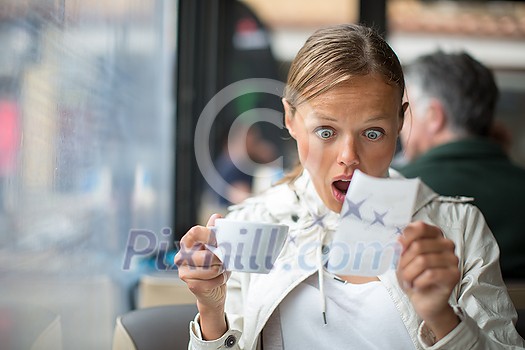 Pretty, young woman baffled with the bill in a coffeeshop/restaurant