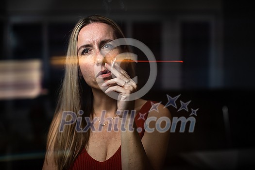 Mid-aged woman lighting a cigarette at home, getting her nicotine daily dose, unable to resist to her unhealthy habit Mid-aged woman lighting a cigarette at home, getting her nicotine daily dose, unable to resist to her unhealthy habit