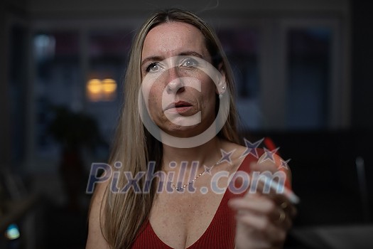 Mid-aged woman lighting a cigarette at home, getting her nicotine daily dose, unable to resist to her unhealthy habit Mid-aged woman lighting a cigarette at home, getting her nicotine daily dose, unable to resist to her unhealthy habit
