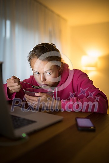 Bad habits concept - young woman paying attention to her smart phone while eating instead of being mindful while at the table