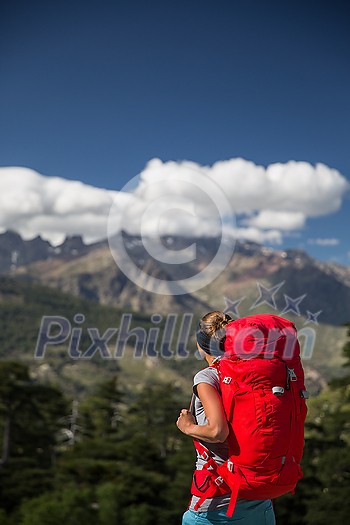 Pretty, female hiker in high mountains packing her backpack