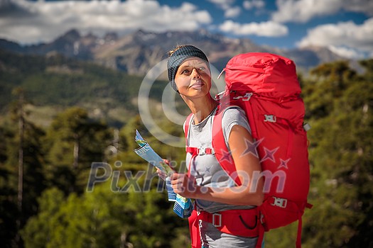 Pretty, female hiker in high mountains using a map to find a way through a mountain range