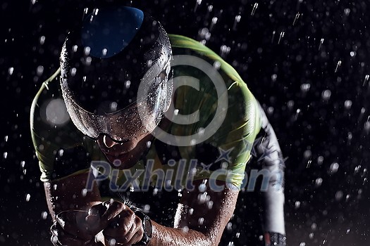 triathlon athlete riding professional racing bike fast  at night with bad weather and falling rain