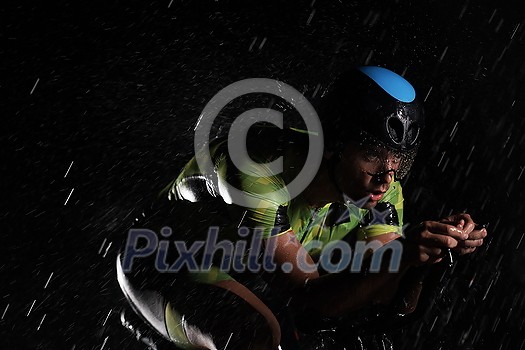 triathlon athlete riding professional racing bike fast at night with bad weather and falling rain triathlon athlete riding professional racing bike fast at night with bad weather and falling rain