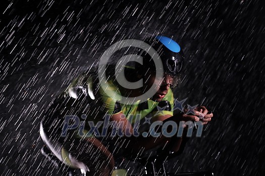 triathlon athlete riding professional racing bike fast  at night with bad weather and falling rain