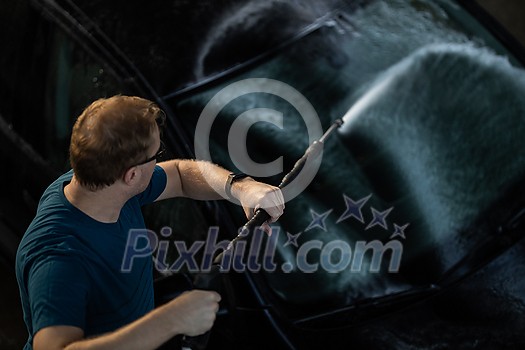 Young man washing his beloved car carefully in a manual car wash to prevent any damage and detail it properly