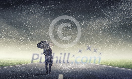Back view of businessman with umbrella and suitcase walking on road Back view of businessman with umbrella and suitcase walking on road