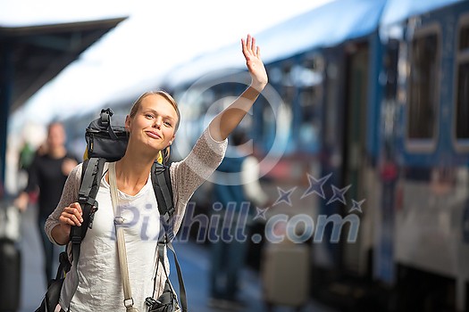 Pretty young woman boarding a train/having arrived to her destination, waiting for her friends to pick her up (color toned image)