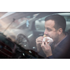 Handsome young man eating a hurried lunch in his car (color toned image; shallow DOF)