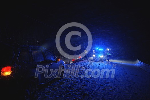 car accident on slippery winter road at night with heavy snow fall and paramedic ambulance first aid car