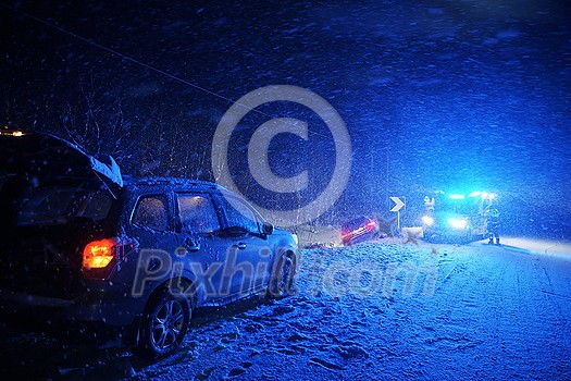 car accident on slippery winter road at night with heavy snow fall and paramedic ambulance first aid car