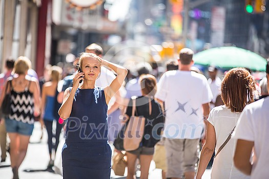 Pretty, young businesswoman talking on the phone while walking in Downtown Manhattan (shallow DOF; color toned image)