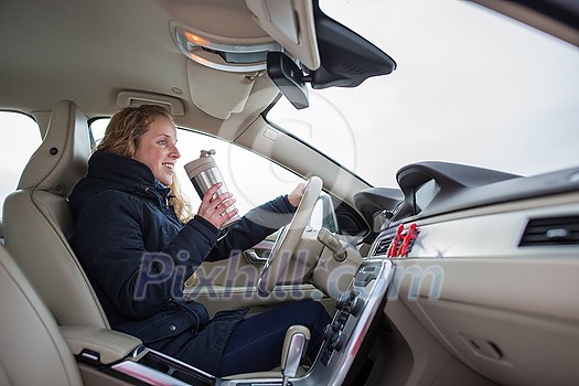 Woman driving a car - female driver at a wheel of a modern car, drinking her morning coffee (shallow DOF; color toned image)