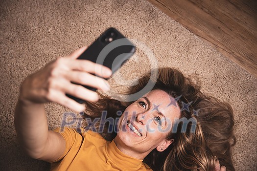 Happy mid-aged woman taking selfie with her smart phone at home Happy mid-aged woman taking selfie with her smart phone at home