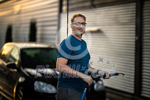Young man washing his beloved car carefully in a manual car wash to prevent any damage and detail it properly Young man washing his beloved car carefully in a manual car wash to prevent any damage and detail it properly