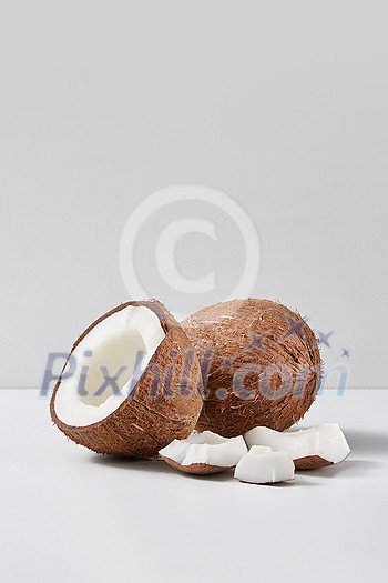 Fresh natural organic ripe whole coconut fruit with half and pieces on a light grey duotone background, copy space. Vegetarian concept. Fresh natural organic ripe whole coconut fruit with half and pieces on a light grey duotone background, copy space. Vegetarian concept.