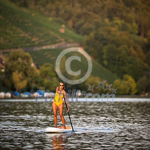 SUP Stand up paddle board concept - Pretty, young woman paddle boarding on a lovely lake in warm late afternoon light - shot from underwater