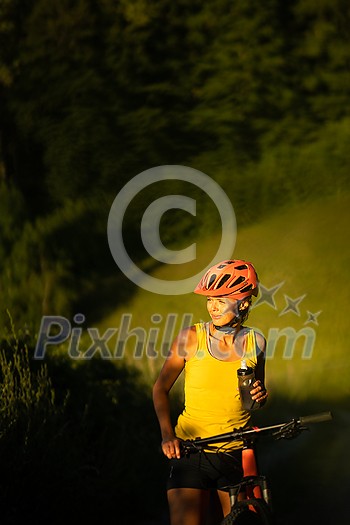 Pretty, young woman biking on a mountain bike enjoying healthy active lifestyle outdoors in summer (shallow DOF)