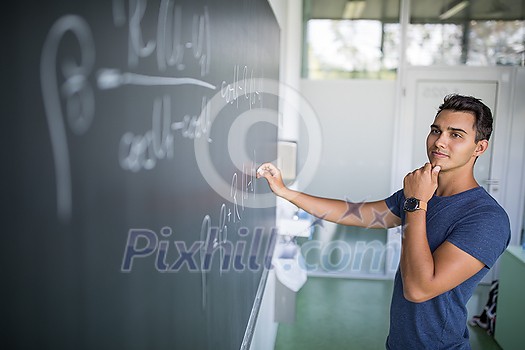 Students in a classroom - handsome student solving a math problem on a blackboard during math class Students in a classroom - handsome student solving a math problem on a blackboard during math class