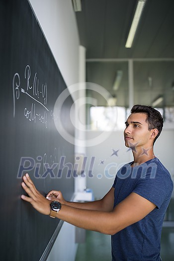 Students in a classroom - handsome student solving a math problem on a blackboard during math class Students in a classroom - handsome student solving a math problem on a blackboard during math class