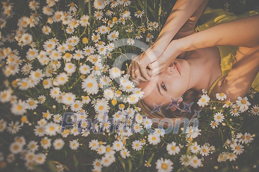 Portrait of young  woman with radiant clean skin lying down amid flowers on a lovely meadow on a spring/summer day