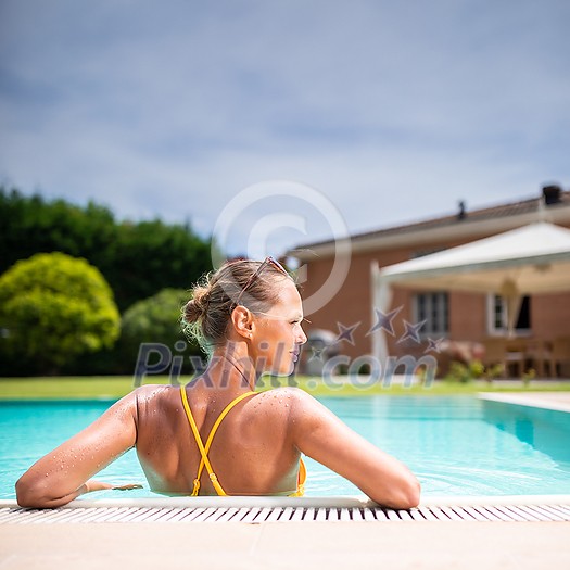 Young Beautiful Suntanned Woman wearing sunglasses relaxing next to a Swimming Pool  on a lovely Summer Day