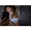 Young woman in bed holding a phone, tired and exhausted, blue light straining her eyes, messing up her circadian rhytm