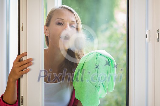 Pretty, young woman washing windows of her household. Cleaning with a detergent (shallow DOF)