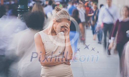 Crowd of people walking on city street - motion blurred image with unrecognizable faces - Young woman standing still, feeling down, depressed