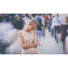 Crowd of people walking on city street - motion blurred image with unrecognizable faces - Young woman standing still, feeling down, depressed