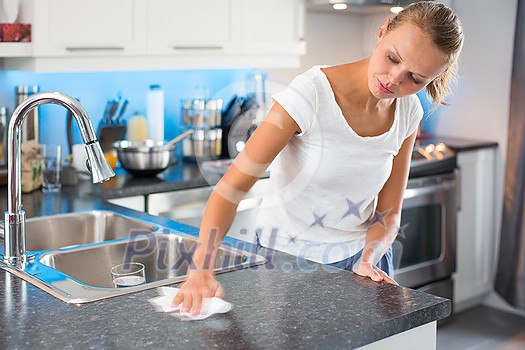 Pretty, young woman in her modern, clean and bright kitchen, cleaning the kitchen (color toned imagey; shallow DOF)