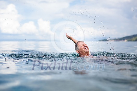 Senior man swimming in the Sea/Ocean - enjoying active retirement, having fun, taking care of himself, staying fit (shallow DOF)