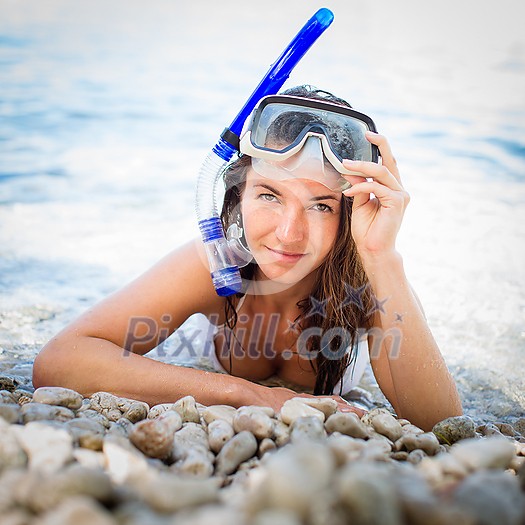 Pretty, young woman on a beach during her summer vacation with snorkel lying on beach with snorkeling mask and fins smiling happy enjoying the sun on a sunny summer day. Pretty, young woman on a beach during her summer vacation with snorkel lying on beach with snorkeling mask and fins smiling happy enjoying the sun on a sunny summer day.