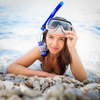 Pretty, young woman on a beach during her summer vacation with snorkel lying on beach with snorkeling mask and fins smiling happy enjoying the sun on a sunny summer day.
