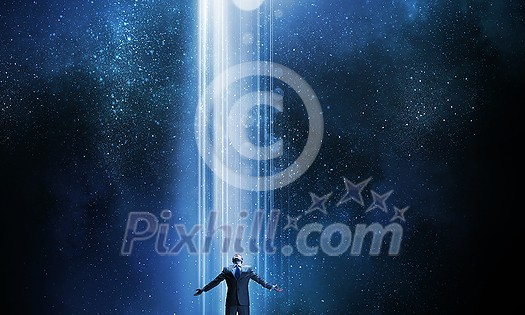 Businessman with hands spread apart standing in light coming from above Businessman with hands spread apart standing in light coming from above