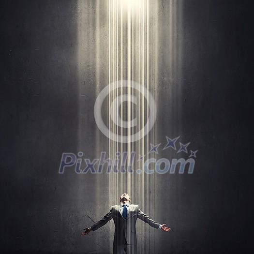 Businessman with hands spread apart standing in light coming from above Businessman with hands spread apart standing in light coming from above