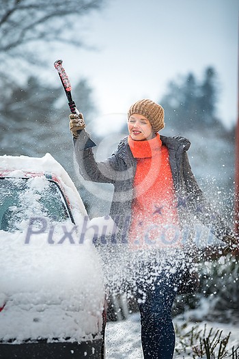 Pretty, young woman cleaning her car from snow after heavy snowstorm (color toned image)