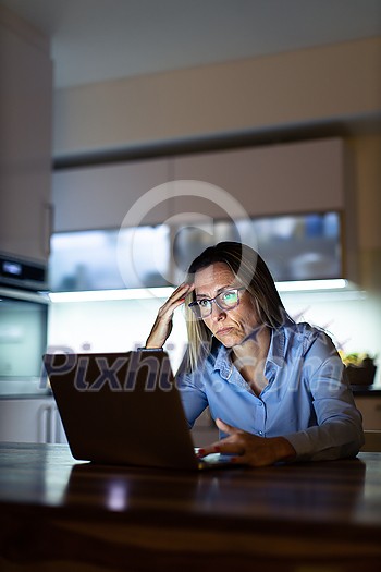 Pretty, middle-aged woman working late in the day on a laptop computer at home, running a business from home, working remotely - getting frustrated