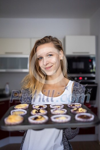 Pretty, young woman baking gluten free cupkes - taking them out of the oven, being pleased with the result