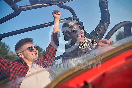 two young happy excited men enjoying beautiful sunny day while driving a off road buggy car on mountain nature