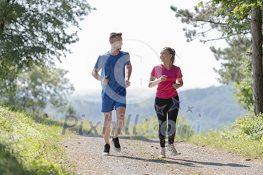 young happy couple enjoying in a healthy lifestyle while jogging on a country road through the beautiful sunny forest, exercise and fitness concept