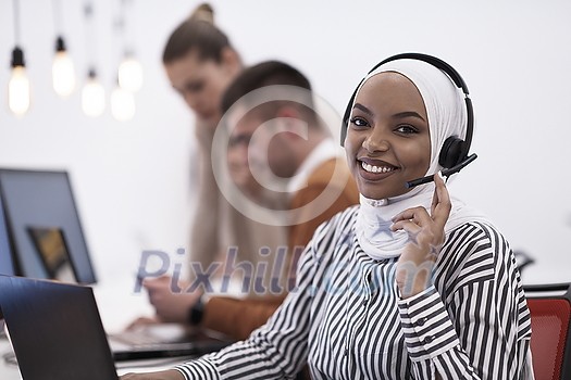 beautiful modern african Muslim businesswoman in office, wearing hijab speaking on headset at modern startup coworking space