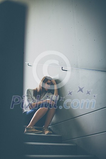 Depressed young woman sitting in a staircase, jobloss due to coronavirus pandemic, Covid-19 outbreak. Unemployment, economic crisis, financial distress concept Depressed young woman sitting in a staircase, jobloss due to coronavirus pandemic, Covid-19 outbreak. Unemployment, economic crisis, financial distress concept