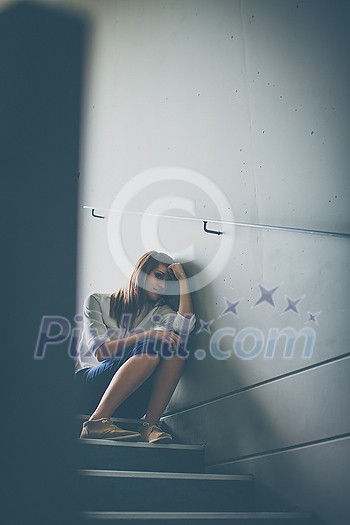 Depressed young woman sitting in a staircase, jobloss due to coronavirus pandemic, Covid-19 outbreak. Unemployment, economic crisis, financial distress concept