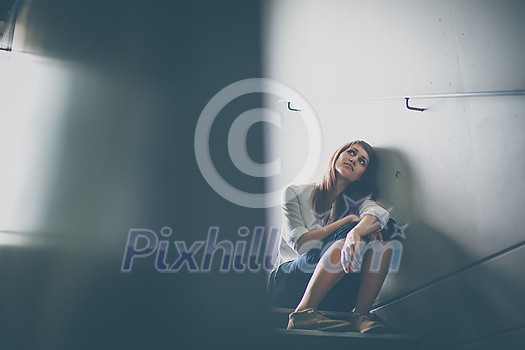 Depressed young woman sitting in a staircase, jobloss due to coronavirus pandemic, Covid-19 outbreak. Unemployment, economic crisis, financial distress concept