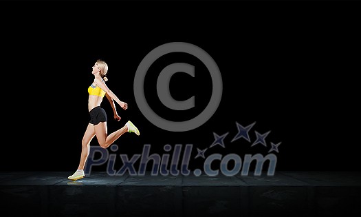 Young woman athlete running fast on dark background 