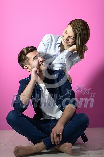 a young couple sitting on the floor while posing in front of a pink background
