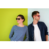 Full ready for summer! Beautiful young loving couple adjusting their sunglasses while standing against green-grey background
