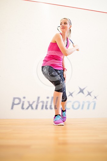 Cute young woman playing squash on a squash court, hitting the ball