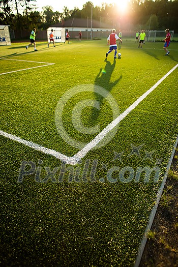 Soccer players on a pitch having match, lit by warm evening sun